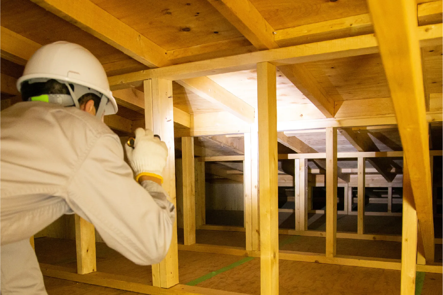 屋根裏でヘルメットを着用し点検するスタッフ