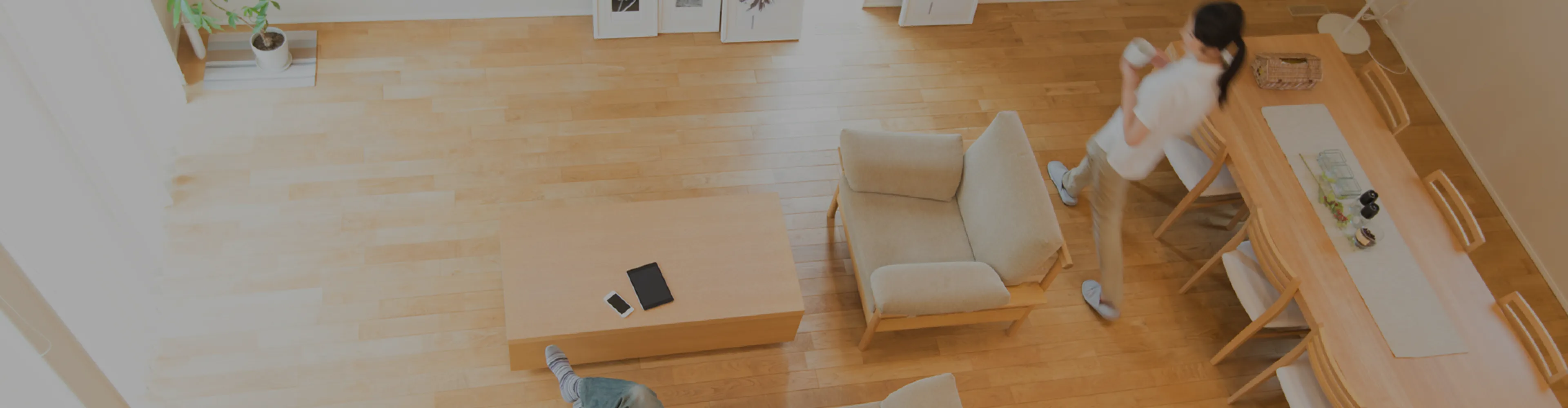 明るいリビングとダイニングの俯瞰写真。木の床、ローテーブルと椅子、食卓、マグを持つ女性。